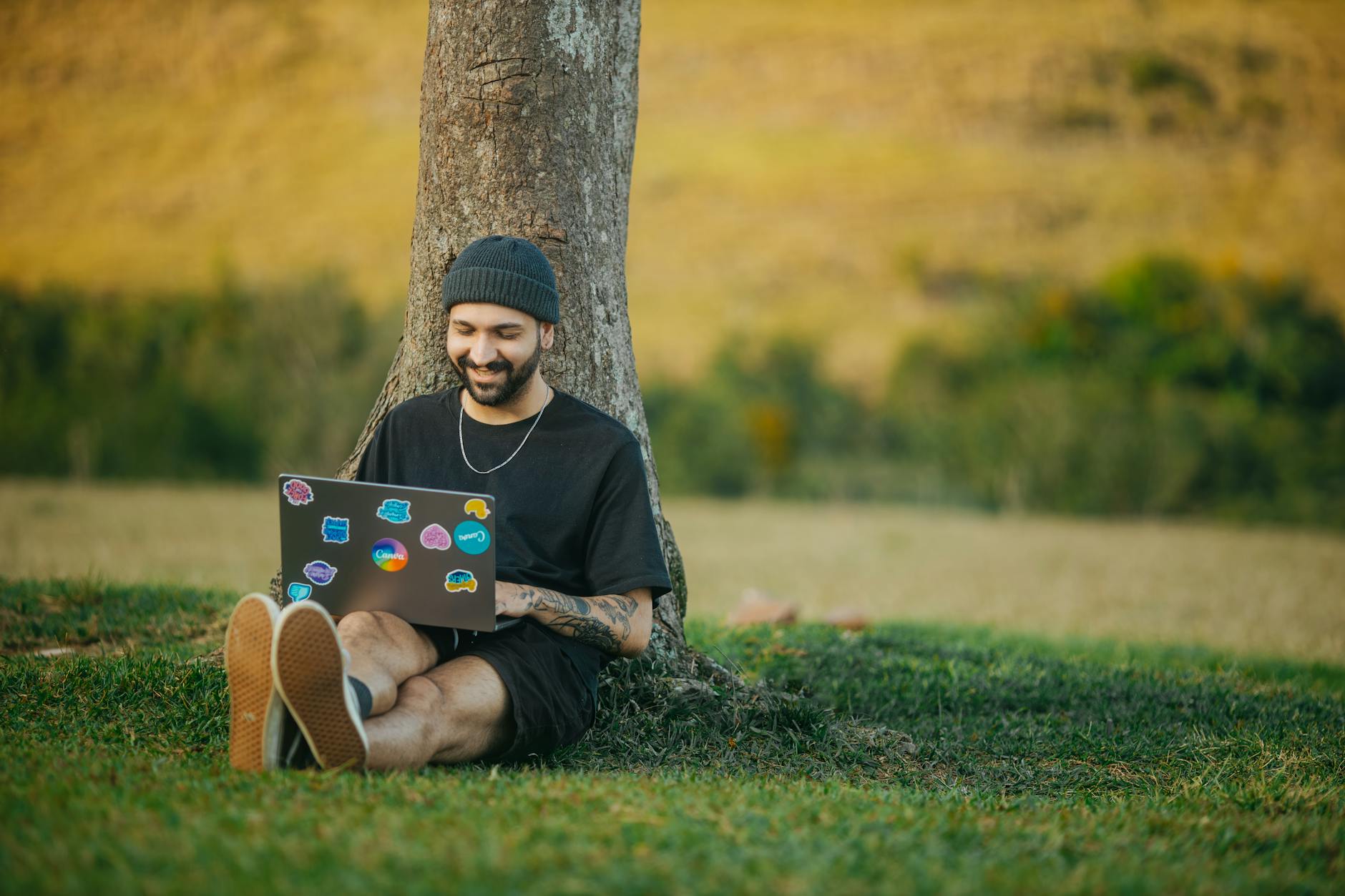 Person working on laptop computer in rural countryside setting with farmland in background