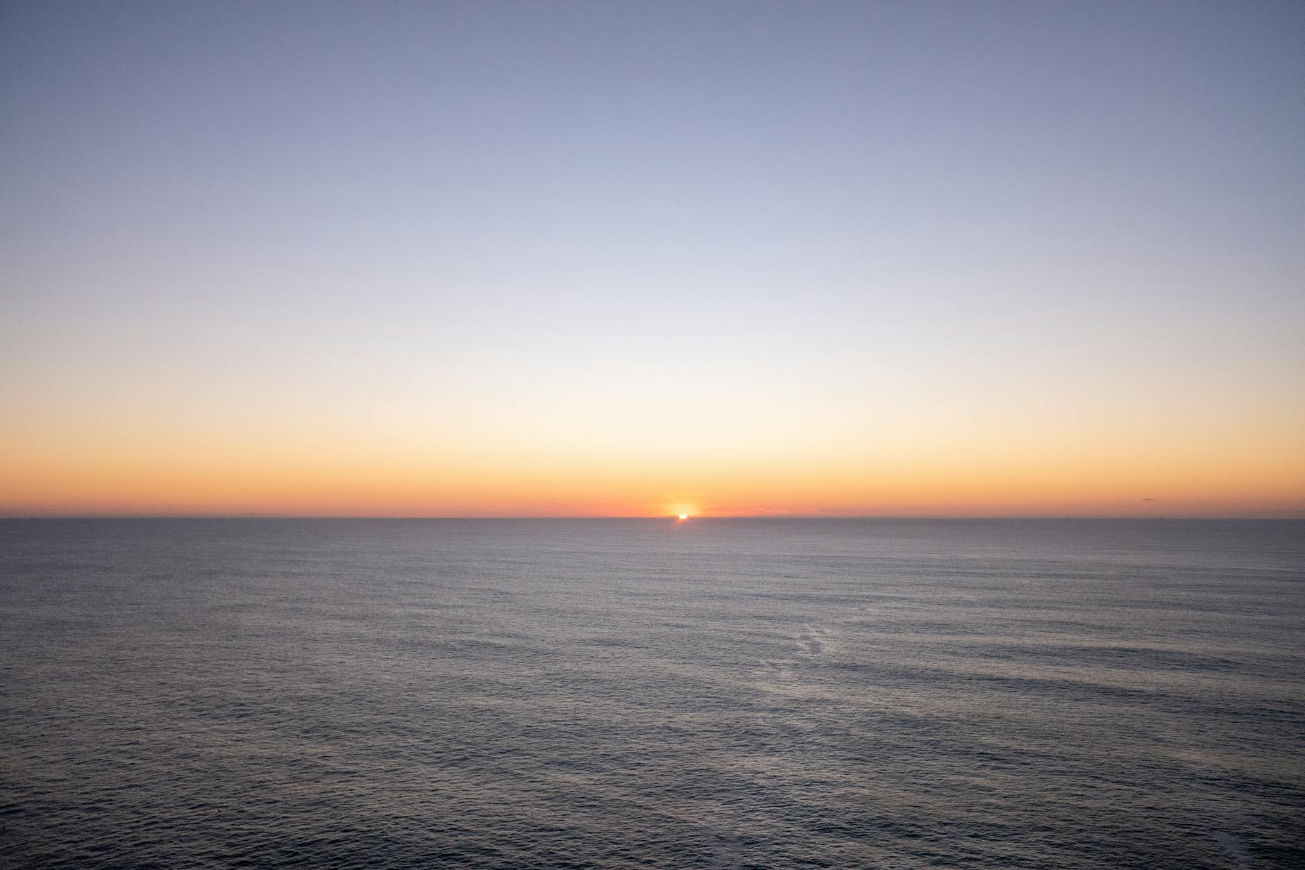 Dramatic sunset over calm ocean waters with silhouetted palm trees