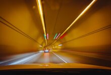 A car driving through a lit urban road tunnel representing toll infrastructure investment