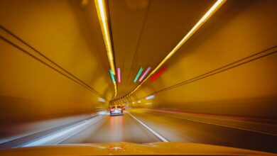 A car driving through a lit urban road tunnel representing toll infrastructure investment