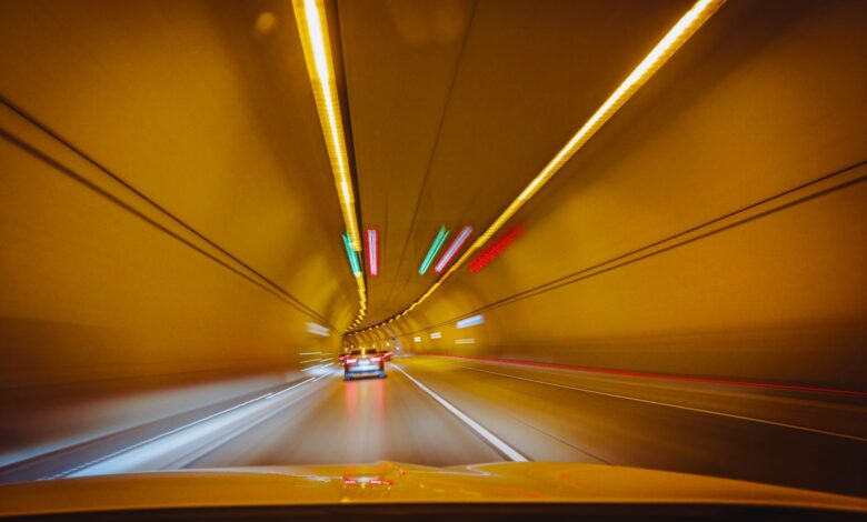A car driving through a lit urban road tunnel representing toll infrastructure investment
