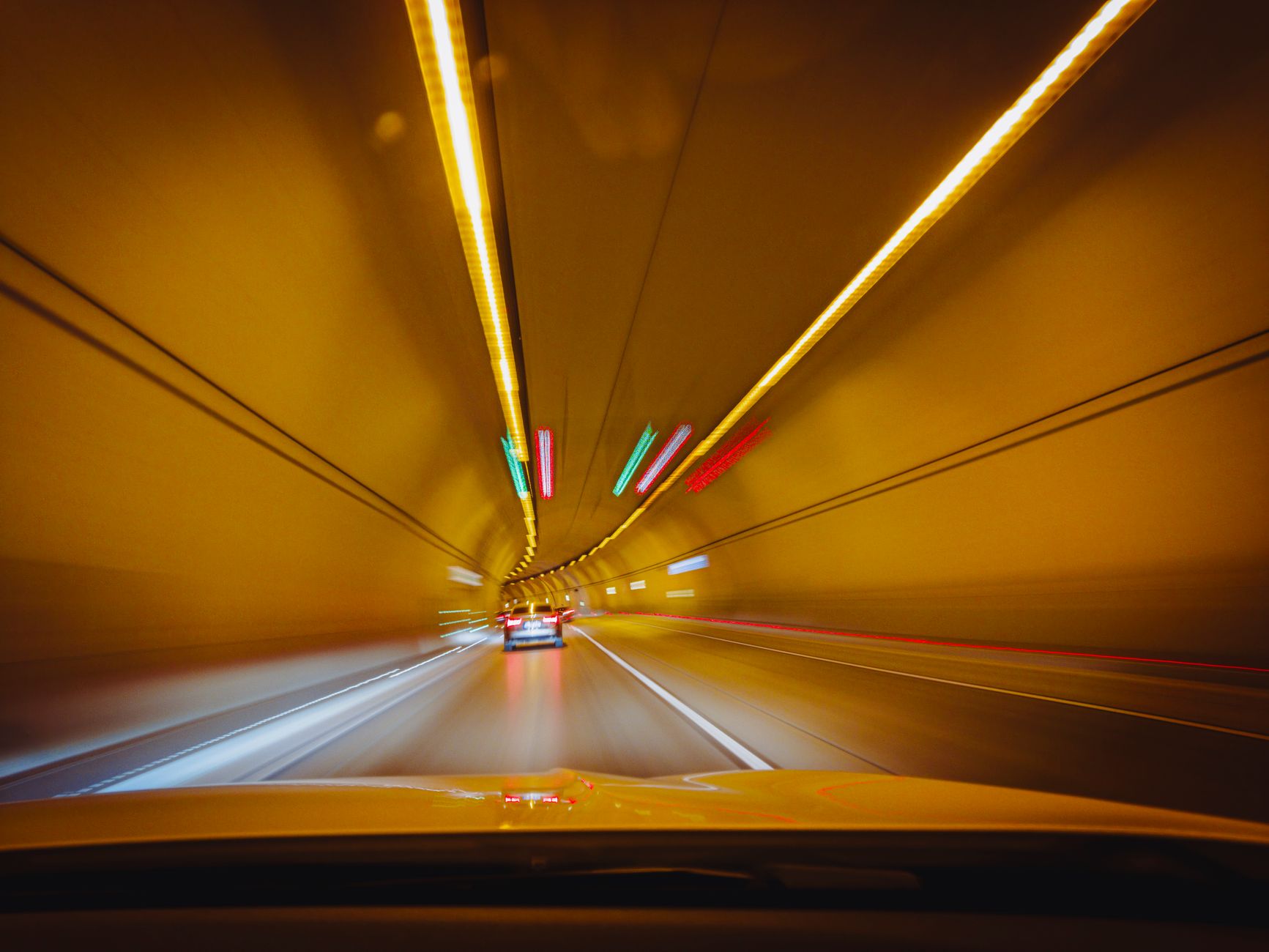 A car driving through a lit urban road tunnel representing toll infrastructure investment