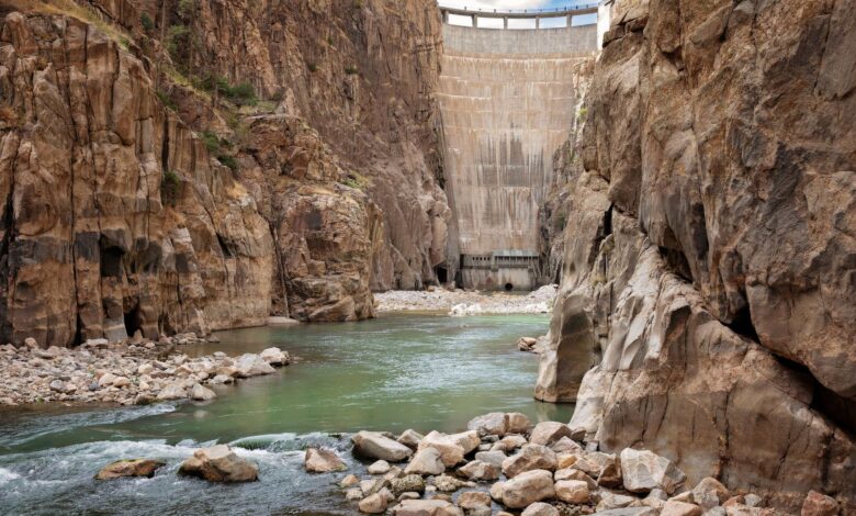 Large hydropower dam with water flowing through spillways and surrounding mountain landscape