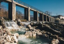 A large hydroelectric dam releasing water through spillways in a mountainous river valley