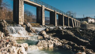 A large hydroelectric dam releasing water through spillways in a mountainous river valley