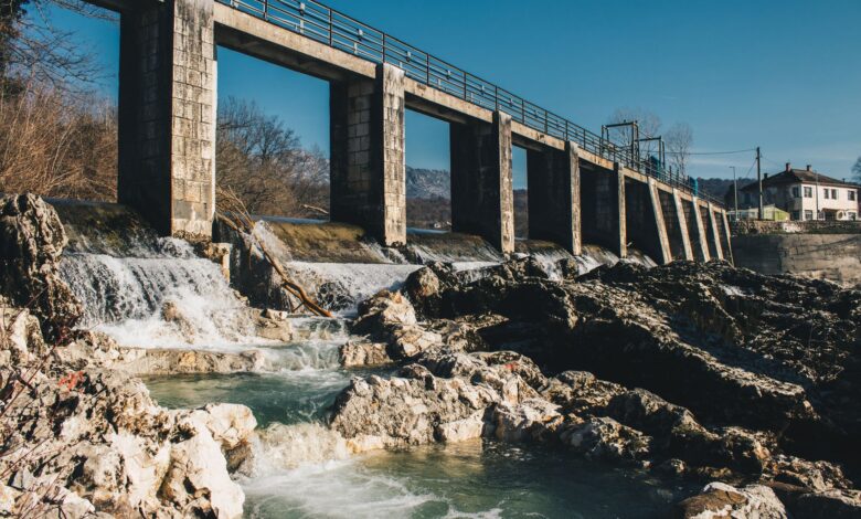 A large hydroelectric dam releasing water through spillways in a mountainous river valley