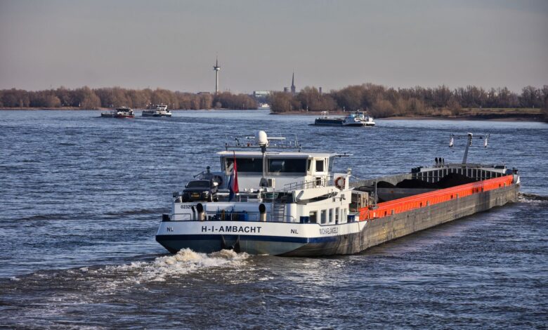 A large barge traveling along an inland waterway near an industrial terminal