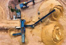 Aerial view of an active sand quarry with excavation equipment and white silica sand piles