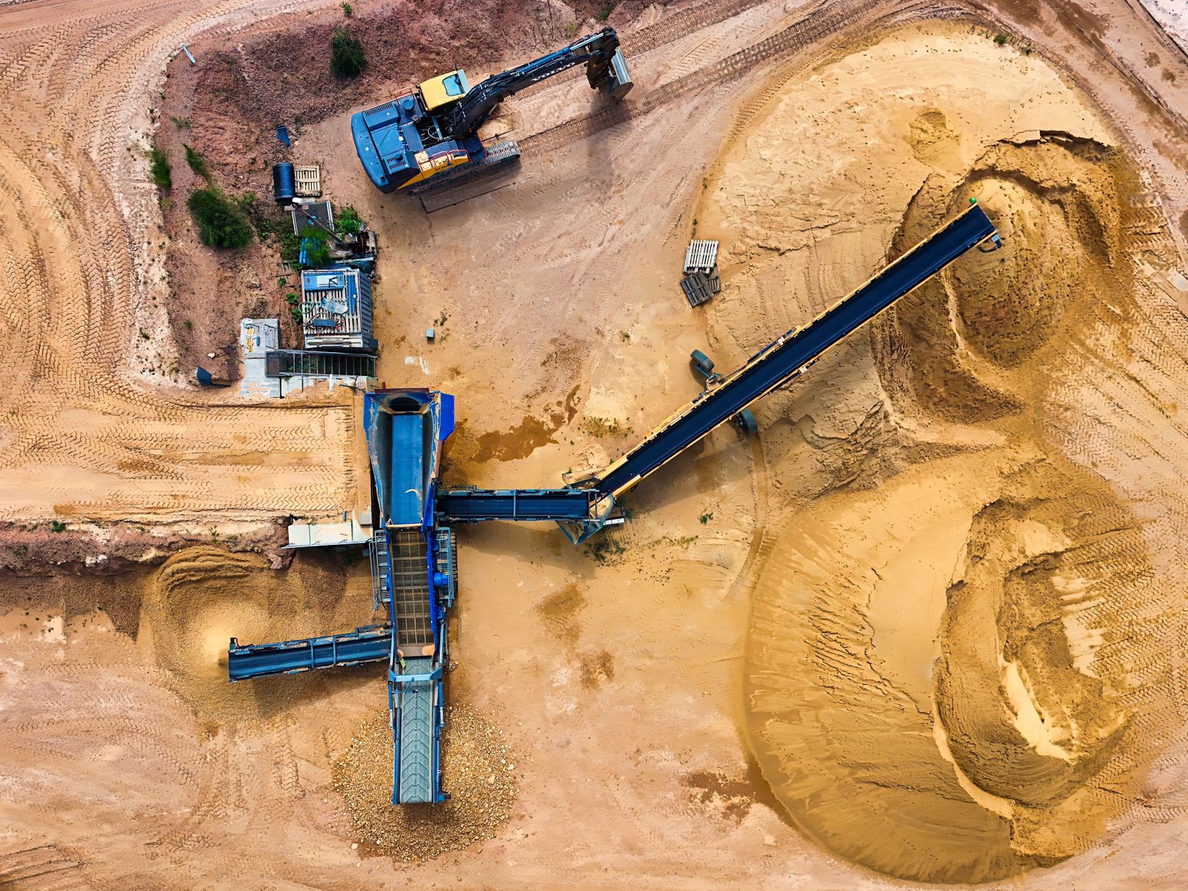 Aerial view of an active sand quarry with excavation equipment and white silica sand piles